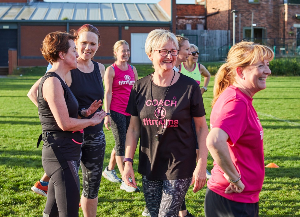 A female coach smiling, surrounded by smiling participants on a sports field.