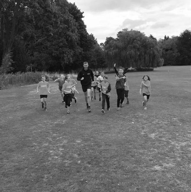 Athletics Leader Alex running towards the camera with a group of young athletes.