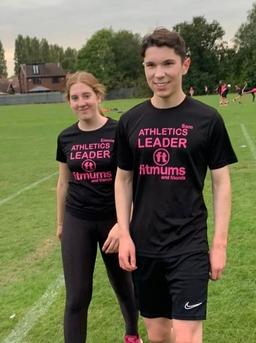 Athletics Leaders Emmie and Sam walking across a sports field in their black Fitmums & Friends t-shirts.