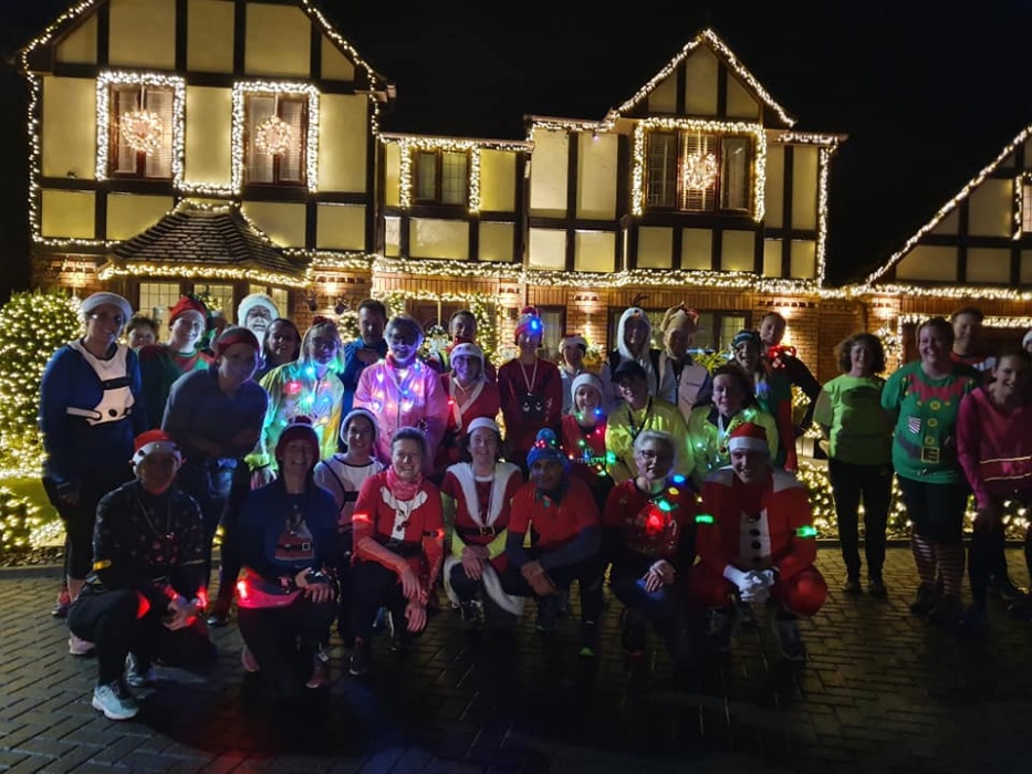 A group of runners in Christmas outfits in front of a house decorated with Christmas lights