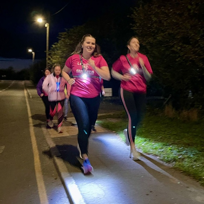 A group of women running together at night, wearing lights.