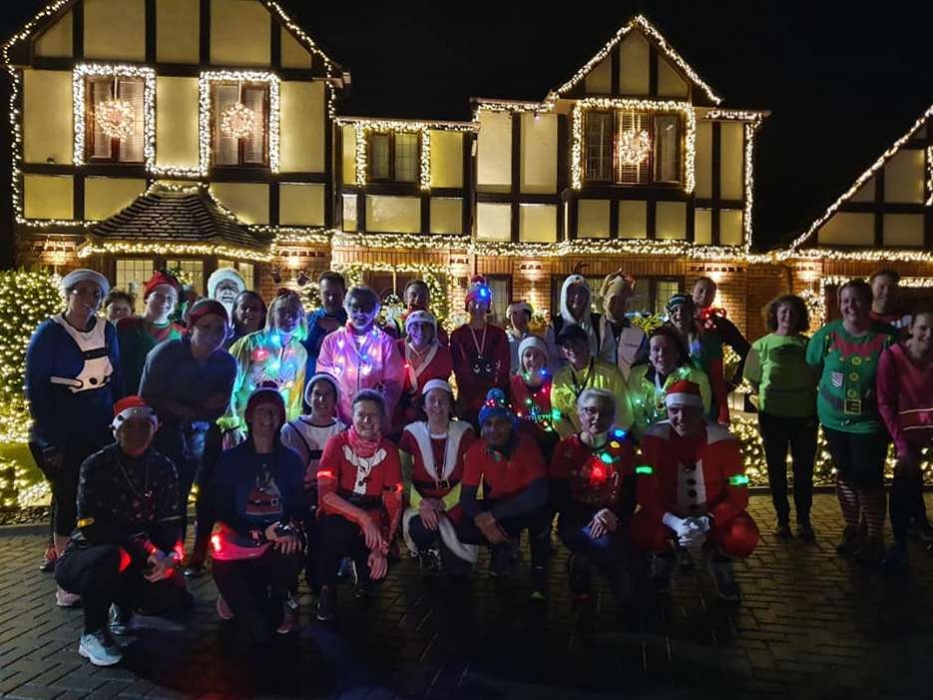 A group of runners in Christmas outfits in front of a house decorated with Christmas lights