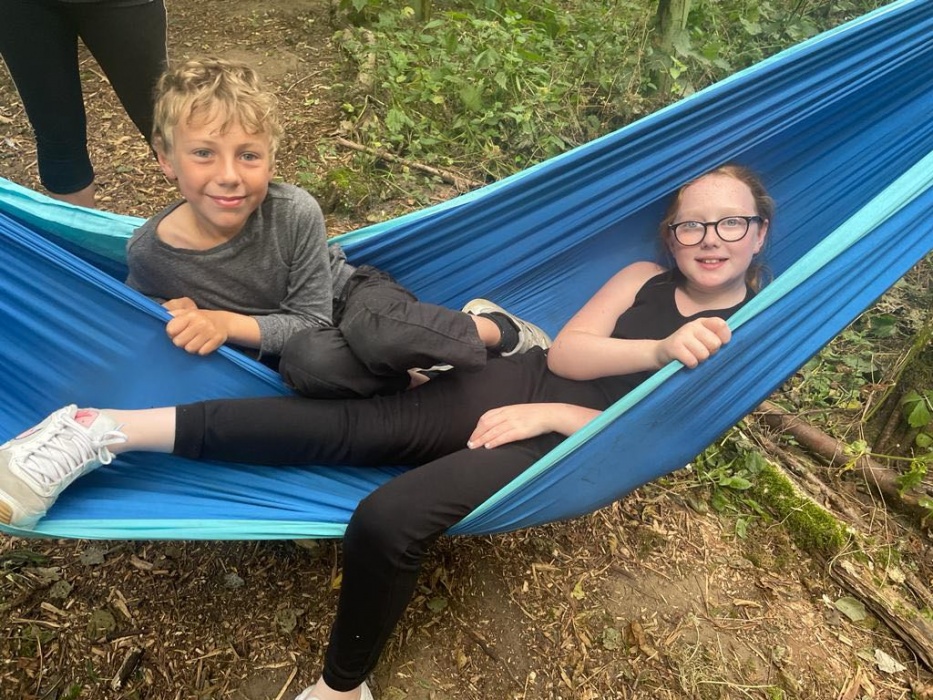 A boy and a girl in a blue hammock in the forest