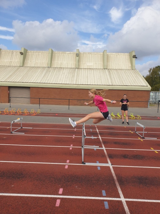 A teen athlete hurdling on an athletics track