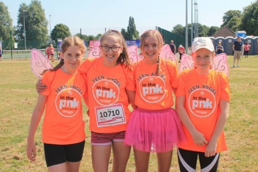 4 teenagers dressed in orange tops and pink wings smiling at the camera